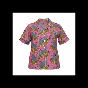 A short-sleeve button-front pajama shirt with a pink base and an allover print of golden lions and blue-gray foliage, shown on a pink background.