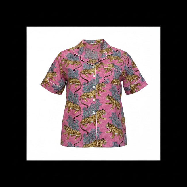A short-sleeve button-front pajama shirt with a pink base and an allover print of golden lions and blue-gray foliage, shown on a pink background.
