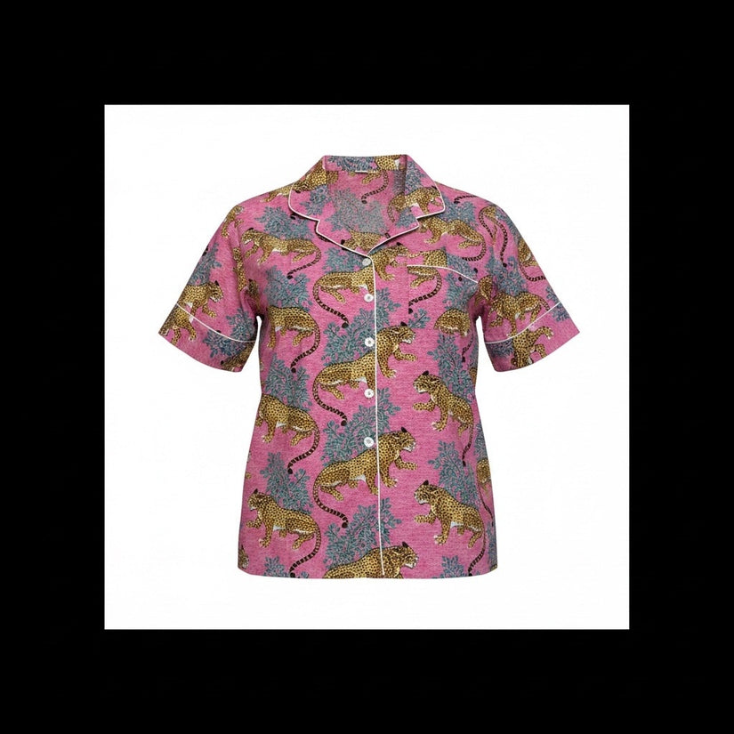 A short-sleeve button-front pajama shirt with a pink base and an allover print of golden lions and blue-gray foliage, shown on a pink background.