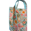 A quilted tote bag with a colorful tropical print featuring palm trees, suns, and flowers, with braided rope handles and a small wooden brand tag reading 'The Palm Tree Co.'.